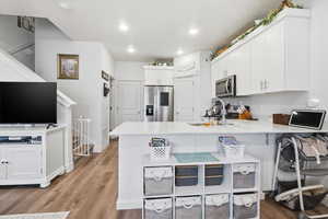 Kitchen featuring a peninsula, white cabinetry, a kitchen breakfast bar, stainless steel appliances, and light wood-type flooring