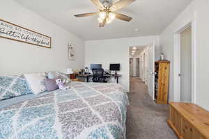 Bedroom with a desk, dark colored carpet, and a ceiling fan
