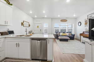Kitchen featuring a peninsula, stainless steel dishwasher, open floor plan, white cabinetry, and recessed lighting