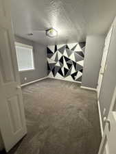 Empty room featuring dark colored carpet, an accent wall, and a textured ceiling