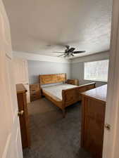 Bedroom with dark carpet, ceiling fan, and a textured ceiling