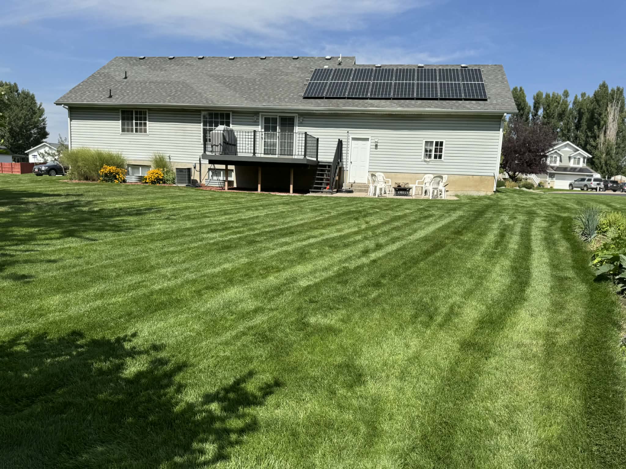 Rear view of property featuring a deck, a lawn, roof mounted solar panels, and a shingled roof