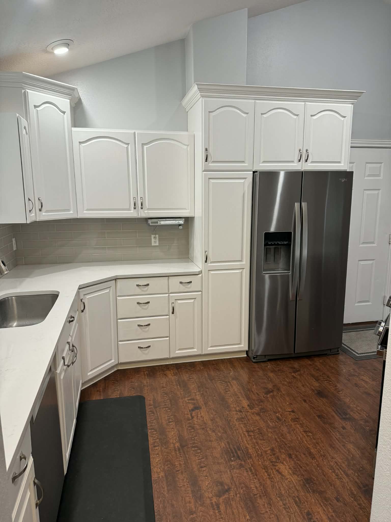 Kitchen with stainless steel appliances, white cabinets, backsplash, dark wood-style floors, and lofted ceiling