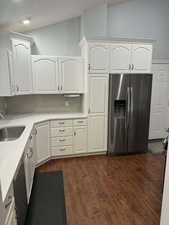 Kitchen with stainless steel appliances, white cabinets, backsplash, dark wood-style floors, and lofted ceiling
