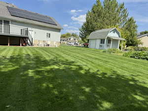 View of green lawn with an outbuilding, a detached garage, a deck, and a patio area