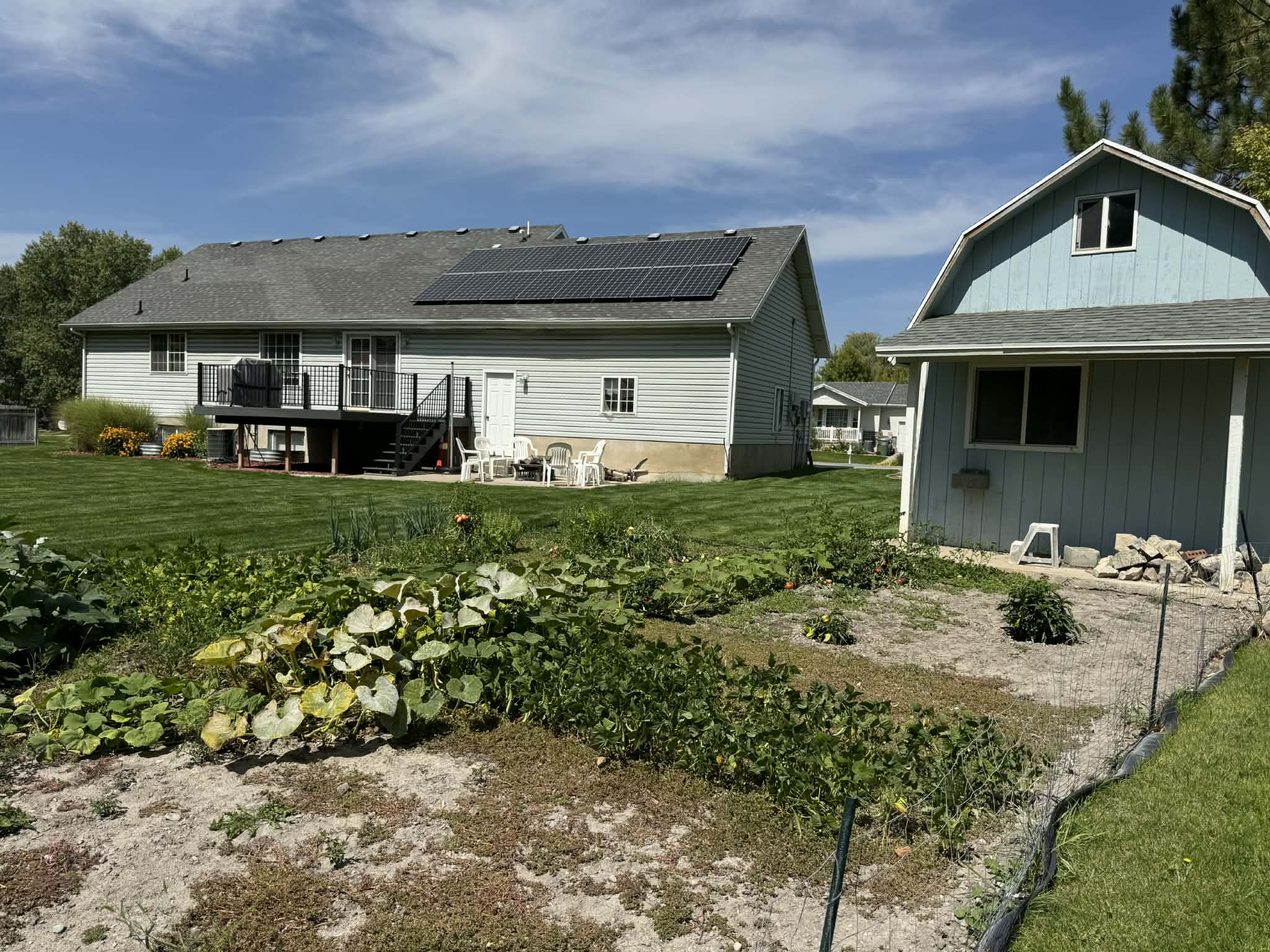 Rear view of house with a shingled roof, solar panels, a yard, a deck, and a gambrel roof