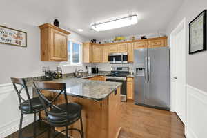 Kitchen with stainless steel appliances, a breakfast bar, a peninsula, dark stone countertops, and a wainscoted wall