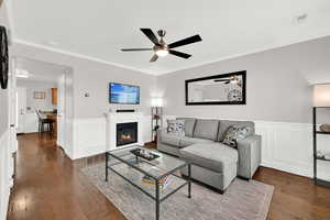 Living room with wainscoting, a glass covered fireplace, crown molding, a decorative wall, and dark wood finished floors