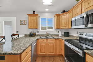 Kitchen featuring stainless steel appliances, a peninsula, dark stone counters, a breakfast bar area, and light wood finished floors