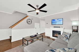 Living area featuring a wainscoted wall, a decorative wall, dark wood-style flooring, a glass covered fireplace, and crown molding