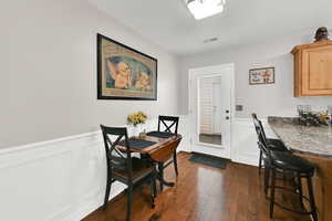 Dining space with wainscoting, dark wood-style flooring, and a decorative wall