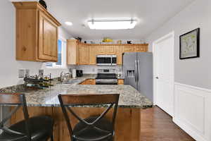 Kitchen featuring a breakfast bar area, stainless steel appliances, dark stone countertops, a peninsula, and dark wood-type flooring