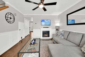 Living area with a decorative wall, wainscoting, dark wood-type flooring, a glass covered fireplace, and ornamental molding