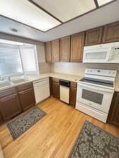 Kitchen featuring light countertops, white appliances, wood finish cabinets, light wood-style flooring, and a textured ceiling