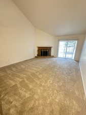 Unfurnished living room featuring a brick fireplace, light colored carpet, and lofted ceiling