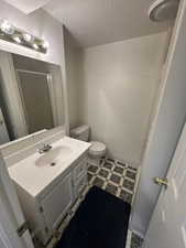 Bathroom featuring vanity, a textured ceiling, light floors, and a shower with shower door