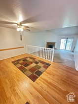 Unfurnished room featuring wood finished floors, a ceiling fan, a fireplace, and a textured ceiling