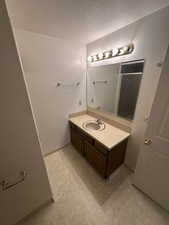 Bathroom featuring a textured ceiling, vanity, light flooring, and light carpet