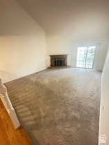Unfurnished living room with a glass covered fireplace, carpet floors, and lofted ceiling