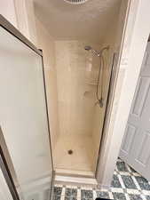 Full bath with a stall shower, a textured ceiling, and light floors
