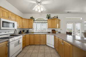 Kitchen featuring white appliances, light tile patterned floors, healthy amount of natural light, and wood finish cabinetry