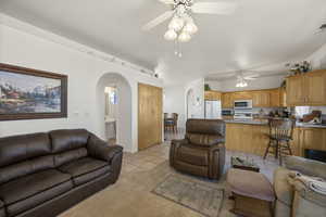 Living area featuring light tile patterned floors, a ceiling fan, arched walkways, and light colored carpet