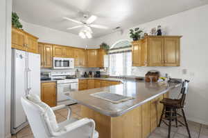 Kitchen with a peninsula, white appliances, light tile patterned floors, ceiling fan, and a kitchen breakfast bar