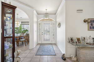 Foyer entrance featuring ornamental molding, light tile patterned flooring, suspended lighting, and arched walkways
