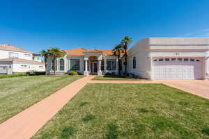 View of front facade with stucco siding, an attached garage, a front yard, driveway, and a tile roof