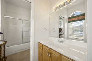 Bathroom featuring vanity, combined bath / shower with glass door, and light carpet