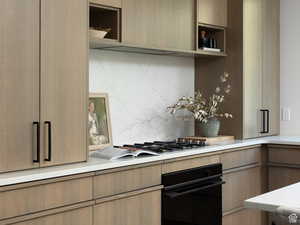 Kitchen with black oven, modern cabinets, tasteful backsplash, open shelves, and stainless steel gas stovetop