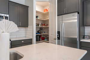 Kitchen featuring backsplash, gray cabinets, stainless steel fridge with ice dispenser, and light stone counters