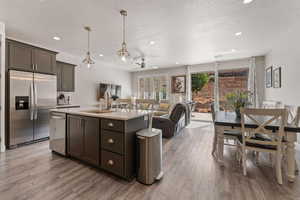 Kitchen featuring stainless steel appliances, pendant lighting, light wood-style floors, ceiling fan, and a center island with sink