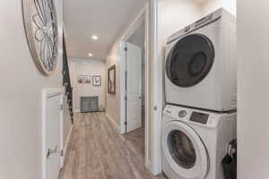 Laundry area featuring light wood-style floors, stacked washing machine and dryer, and recessed lighting