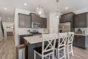 Kitchen with light wood-style floors, an island with sink, stainless steel appliances, and light stone counters