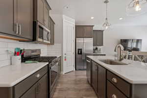 Kitchen featuring stainless steel appliances, a kitchen island with sink, hanging light fixtures, light stone counters, and dark wood-style flooring