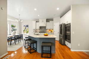 Kitchen featuring light wood finished floors, an island with sink, stainless steel appliances, a chandelier, and a kitchen bar