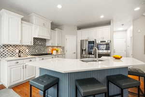 Kitchen featuring a breakfast bar, quartz counters, stainless steel appliances, a large island with sink, pantry, and recessed lighting