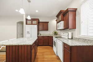 Second kitchen featuring white appliances, arched walkways, light wood finished floors, a kitchen island, and glass fronted cabinets