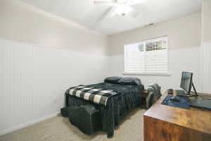 Bedroom with a wainscoted wall, a desk, a textured ceiling, wooden walls, and ceiling fan