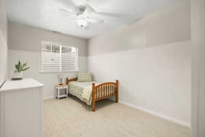 Bedroom featuring wainscoting, a ceiling fan, a textured ceiling, light colored carpet, and wooden walls