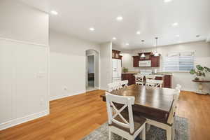 Dining room with arched walkways, wainscoting, light wood finished floors, and recessed lighting