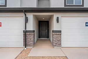 Entrance to property featuring stone siding, stucco siding, and an attached garage