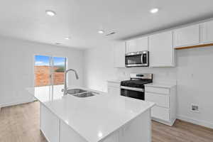 Kitchen with stainless steel appliances, white cabinetry, a center island with sink, light wood-type flooring, and recessed lighting