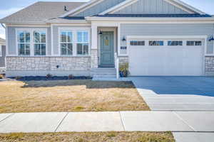 View of front of home featuring board and batten siding, stone siding, roof with shingles, concrete driveway, and a garage