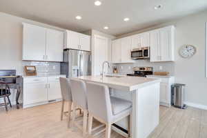 Kitchen featuring stainless steel appliances, white cabinetry, a kitchen bar, light wood-type flooring, and recessed lighting