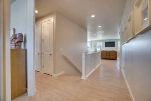 Hall with an upstairs landing, light wood finished floors, and recessed lighting