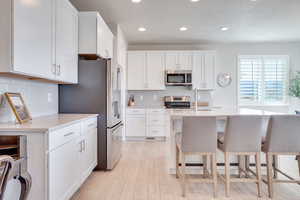 Kitchen with an island with sink, white cabinets, light wood-style floors, stainless steel appliances, and a breakfast bar