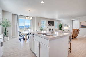 Kitchen featuring a kitchen island with sink, white cabinetry, open floor plan, dishwasher, and light wood finished floors