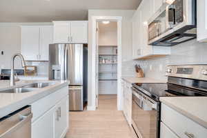 Kitchen with stainless steel appliances, white cabinetry, light wood-style floors, and light stone counters